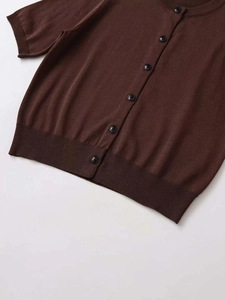 Detail of ribbed hem and black button closure on a dark brown short sleeve knit cardigan