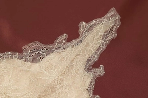 Detailed macro view of ivory lace trim overlay on wine red satin fabric skirt