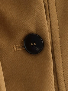 Makroaufnahme des karamellfarbenen Trenchcoats mit Köperbindung und schwarzem Knopf