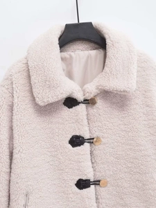 Detail of cream sherpa jacket with golden metal buttons and black leather trim accents