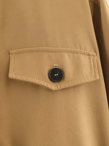 Detail eines khakifarbenen Trenchcoats mit Pattentasche und schwarzem Knopf aus Twill