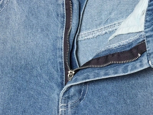 Detail of high-waist light blue denim jeans with silver metal zipper and twill fabric texture