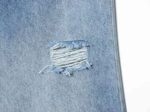 Macro shot of light blue twill denim fabric with distressed ripped hole detail