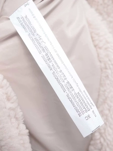 Macro detail of the care label and 100% cotton fabric texture on a fuzzy beige jacket