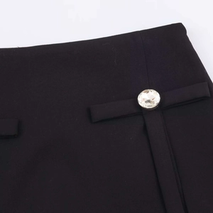 Dettaglio di gonna-pantalone nera a trapezio con fiocco decorativo e fibbia di cristallo