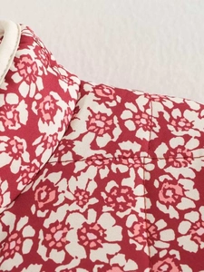 Macro detail of red floral printed quilted jacket with white piped neckline trim