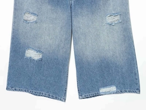 Detail of high-waist light blue denim jeans with distressed ripped holes and white fraying