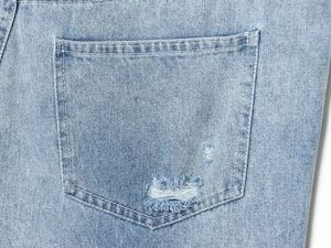 Close-up of light blue denim fabric showing distressed hole detail and back pocket