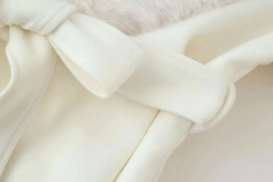 Detail of a creamy white wool coat featuring a decorative bow belt and soft faux fur collar