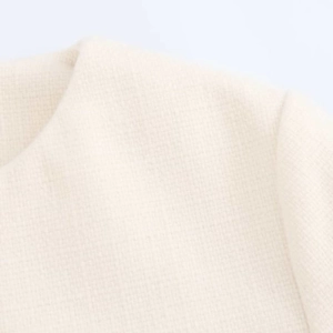 Close-up of beige tweed jacket fabric texture showing woven shoulder and neckline details