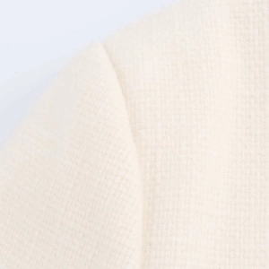 Detailed macro view of ivory tweed fabric texture and shoulder stitching on short jacket