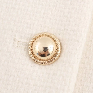 Detailed close-up of a golden dome button with spiral texture on white tweed jacket