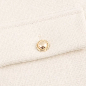 Close-up of golden dome button on cream tweed jacket with detailed textured weaving