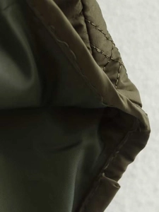 Détail du tissu matelassé à losanges vert olive avec coutures de la veste à capuche