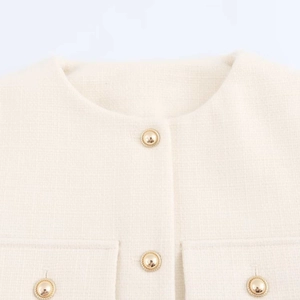 Detail of tweed fabric texture and decorative gold buttons on a cream short jacket