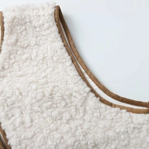 Detail of white faux shearling vest with brown contrast binding and metal zipper closure