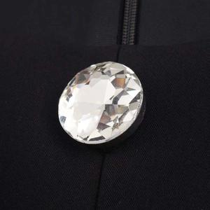Macro detail of a large multifaceted crystal button sewn on black twill fabric with zipper