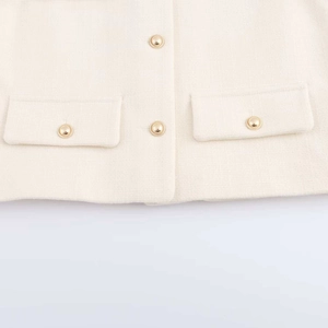 Detail of cream tweed jacket showing textured fabric and embossed gold metal buttons