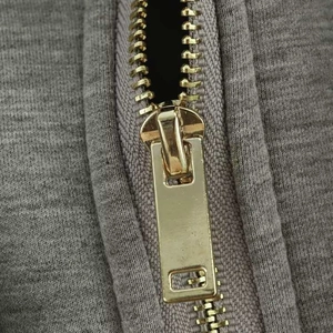 Gros plan de la fermeture éclair dorée sur une veste à capuche matelassée grise