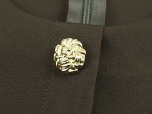 Detailed macro view of an intricate golden woven metal button on deep brown midi dress fabric