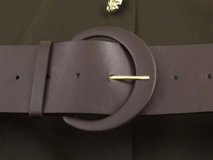 Close-up of a wide dark brown faux leather belt with a large round buckle and gold pin