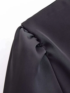 Detailed macro view of pleated shoulder design on a black satin texture blouse