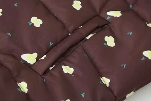 Detail of floral print on dark brown quilted jacket with white petals and yellow centers