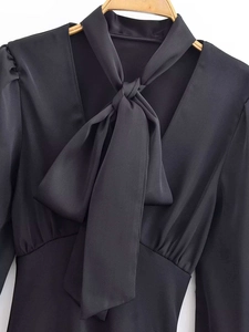 Close-up of black satin long sleeve shirt featuring a bow tie V-neckline and waist detail