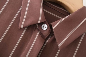Dettaglio del colletto e bottone bianco su una camicia tessuta a righe marroni e bianche