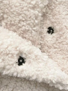 Gros plan sur la texture sherpa blanc cassé avec deux boutons-pression en métal noir