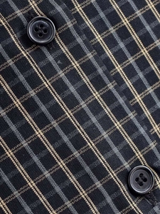 Détail de la texture tissée à carreaux avec boutons en résine noire sur une chemise décontractée