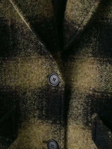 Macro detail of plaid wool coat showing green check pattern and black resin button