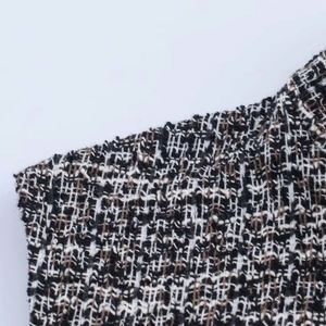 Close-up of grey tweed fabric with interwoven black, white, and brown textured fibers