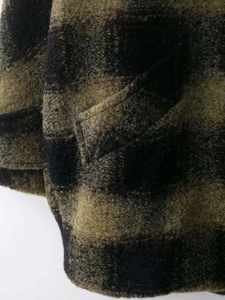 Detail view of the black and green plaid wool coat with brushed texture and flap pocket