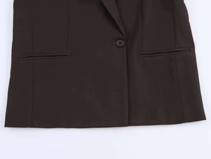 Dettaglio di un blazer marrone scuro con chiusura a un bottone e tasche a filetto simmetriche