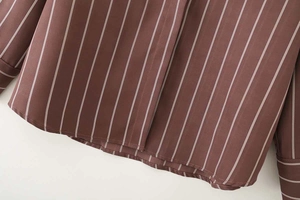 Dettaglio dell'orlo e del polsino di una camicia a righe verticali marrone scuro