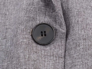 Detail of grey herringbone fabric texture and black resin button on suit jacket