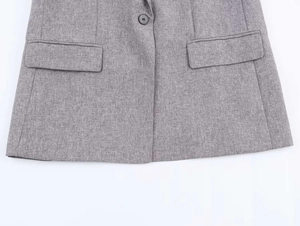 Detail shot of grey herringbone blazer with black button and symmetrical flap pockets