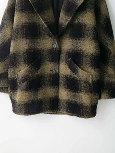 Detail view of olive green and black plaid wool coat with buttons and large pockets