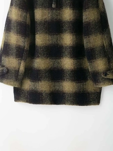 Close-up detail of green and black buffalo check wool coat featuring premium textured fabric