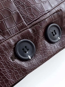 Détail du tissu en similicuir marron foncé à motif crocodile avec des boutons noirs