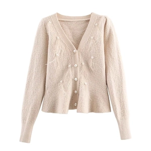 Detail of beige knit cardigan featuring pearl buttons and delicate feather fringe accents