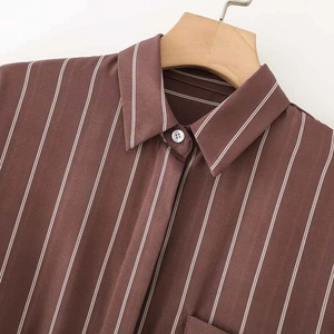 Camicia marrone a righe verticali con colletto classico appesa a una gruccia in legno