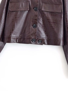 Détail d'une veste en similicuir marron foncé à motif crocodile avec poches à rabat
