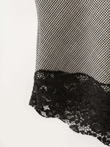 Close-up of houndstooth pattern top featuring delicate black floral lace hem detailing
