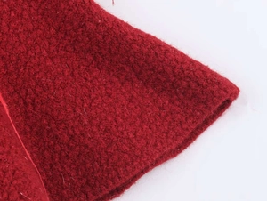 Detail shot of deep red knit sweater fabric showing soft textured bouclé wool material