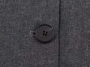 Macro detail of dark grey textured fabric and black four-hole button on this blazer