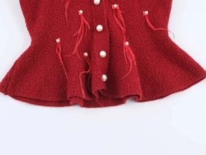 Detail of red knit top featuring pearl embellishments and feather tassel trim