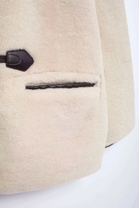 Primer plano detallado del abrigo de piel sintética beige con ribetes de cuero marrón