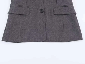 Detail shot of a dark grey textured blazer featuring two flap pockets and a black button